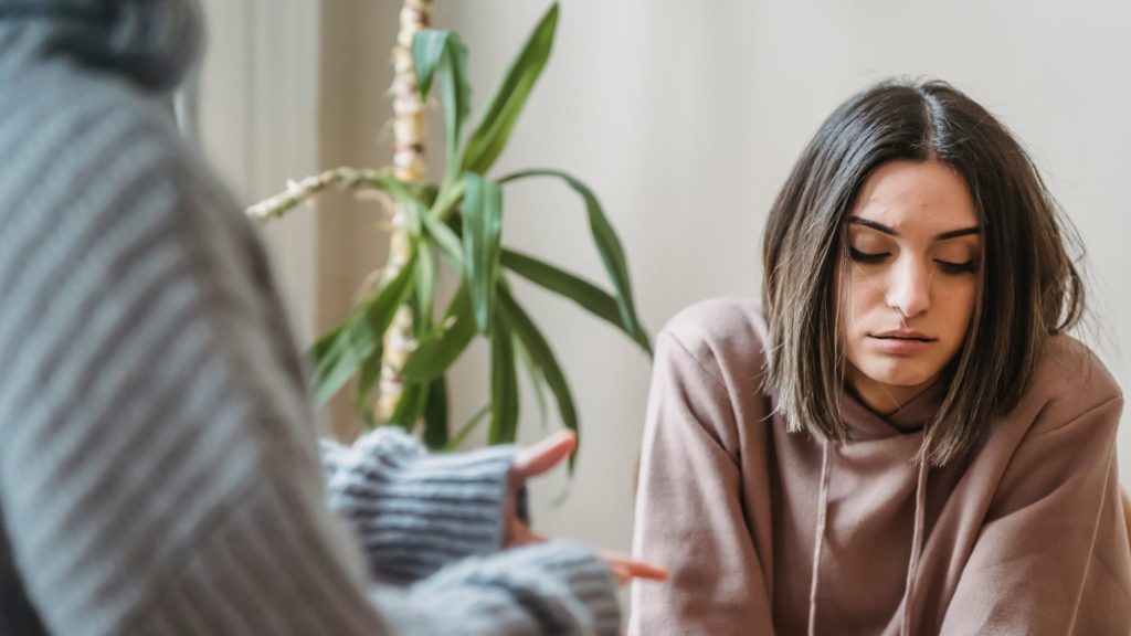 A coworker looks sad or sullen, looking down, as her coworker tries to explain her criticism. They are having a difficult conversation, but trying to employ empathy and curiosity to disarm defensiveness